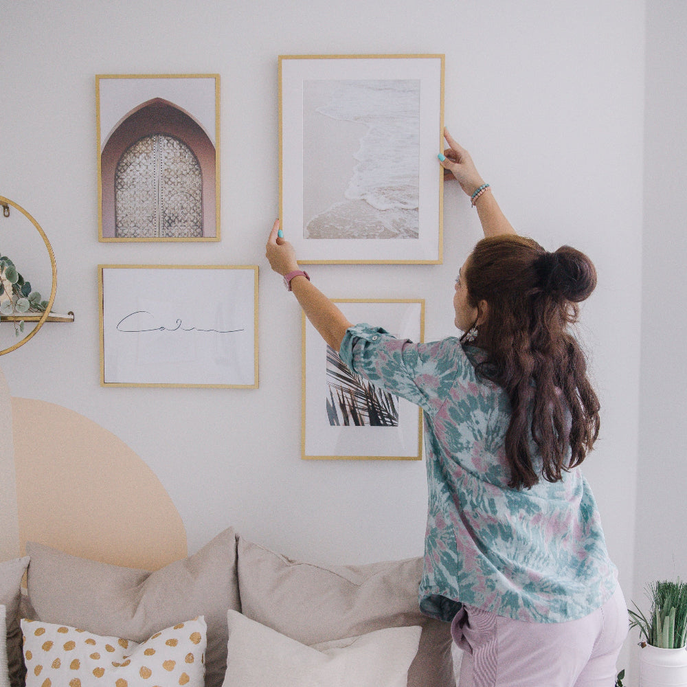 Woman arranging framed pictures on a wall in a bedroom
